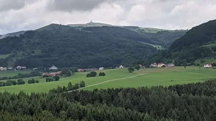 Blick zur Wasserkuppe mit der Radarkuppel, davor Wiesen, Höfe und Nadelwald