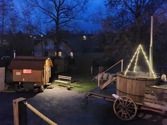 Der Hot Tub mit Lichterkette und die beleuchtete Fasssauna im Hof unter blauem Abendhimmel