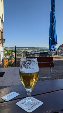 Ein Glas Bier auf dem Tisch der Gasthausterrasse, dahinter der Blick ins Tal