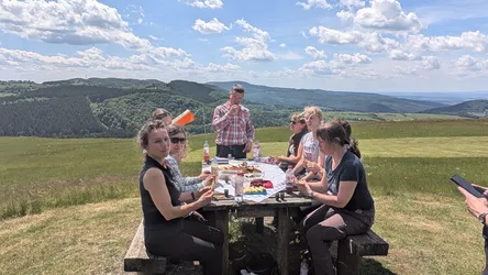 Die Gruppe sitzt am Picknicktisch auf dem Simmelsberg, dahinter die weite Rhönlandschaft