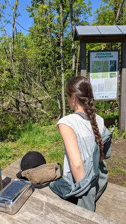 Eine Reiterin liest die Informationstafel am Rastplatz, daneben Helm und Satteltasche