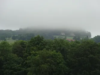 Ein bewaldeter Berg mit einzelnen Häusern verschwindet in der tief hängenden Wolke