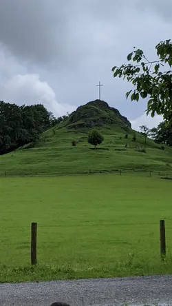Der Wachtküppel mit dem Gipfelkreuz erhebt sich über die Weide, davor ein Stacheldrahtzaun