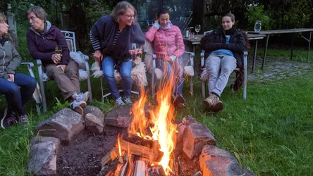 Fünf Frauen sitzen am Abend um das Lagerfeuer im Garten, eine hält ein Weinglas