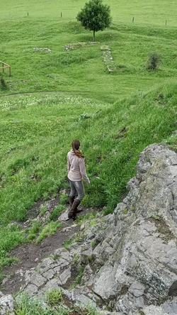 Jemand steigt über die nassen Felsstufen des Wachtküppels ab, unten liegen Grundmauern im Gras