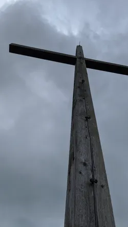 Das hölzerne Gipfelkreuz des Wachtküppels von unten gegen den bewölkten Himmel