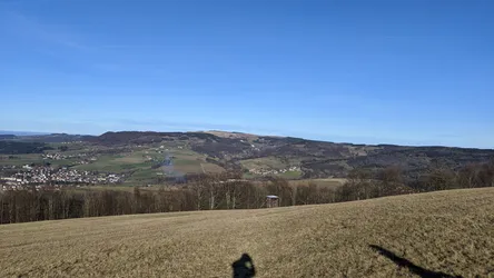 Weiter Blick über ein winterliches Feld auf Hettenhausen im Tal, dahinter die Höhen der Rhön