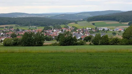 Weiter Blick über Wiesen und Felder auf Thalau im Tal, dahinter die bewaldeten Kuppen der Rhön