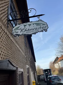 Schmiedeeisernes Schild „Die Rhönreiter“ an der schindelverkleideten Hauswand des Hofes