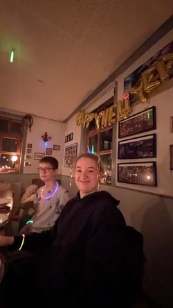 Zwei Jugendliche mit Knicklichtern im Gastraum, im Hintergrund der Schriftzug „Happy New Year“ aus goldenen Ballons