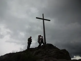 Drei Menschen als Silhouetten am Gipfelkreuz des Wachtküppels unter dunklen Wolken
