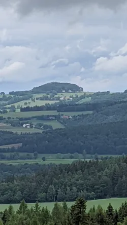 Blick über bewaldete Höhen auf eine ferne Kuppe mit einzelnen Häusern
