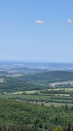 Weiter Blick vom Aussichtsturm über bewaldete Hügel bis zu einer Stadt am Horizont