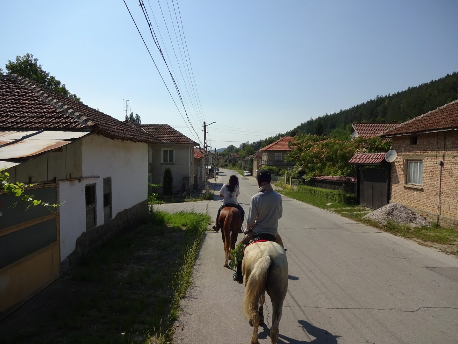 Zwei Reiter auf der Dorfstraße eines bulgarischen Dorfes zwischen niedrigen Wohnhäusern