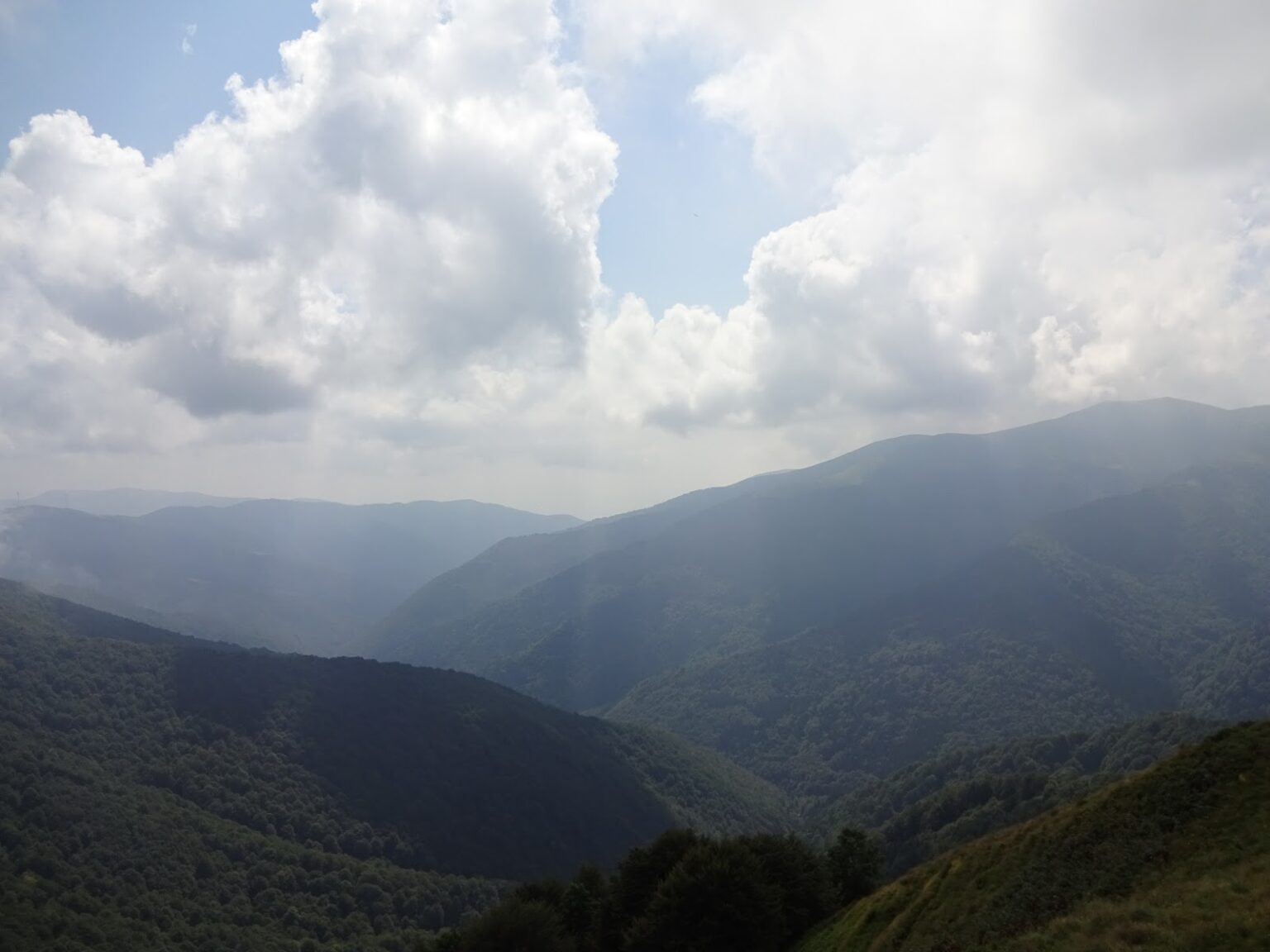 Wolkenspiel über einem Bergtal, einzelne Sonnenstrahlen brechen durch die Wolkendecke auf die bewaldeten Hänge