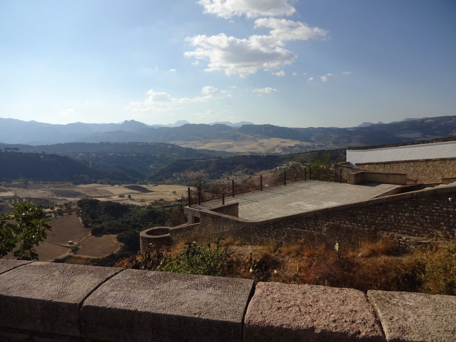 Blick über eine Mauer und die Dächer eines Gehöfts auf die dahinterliegenden Bergketten Andalusiens