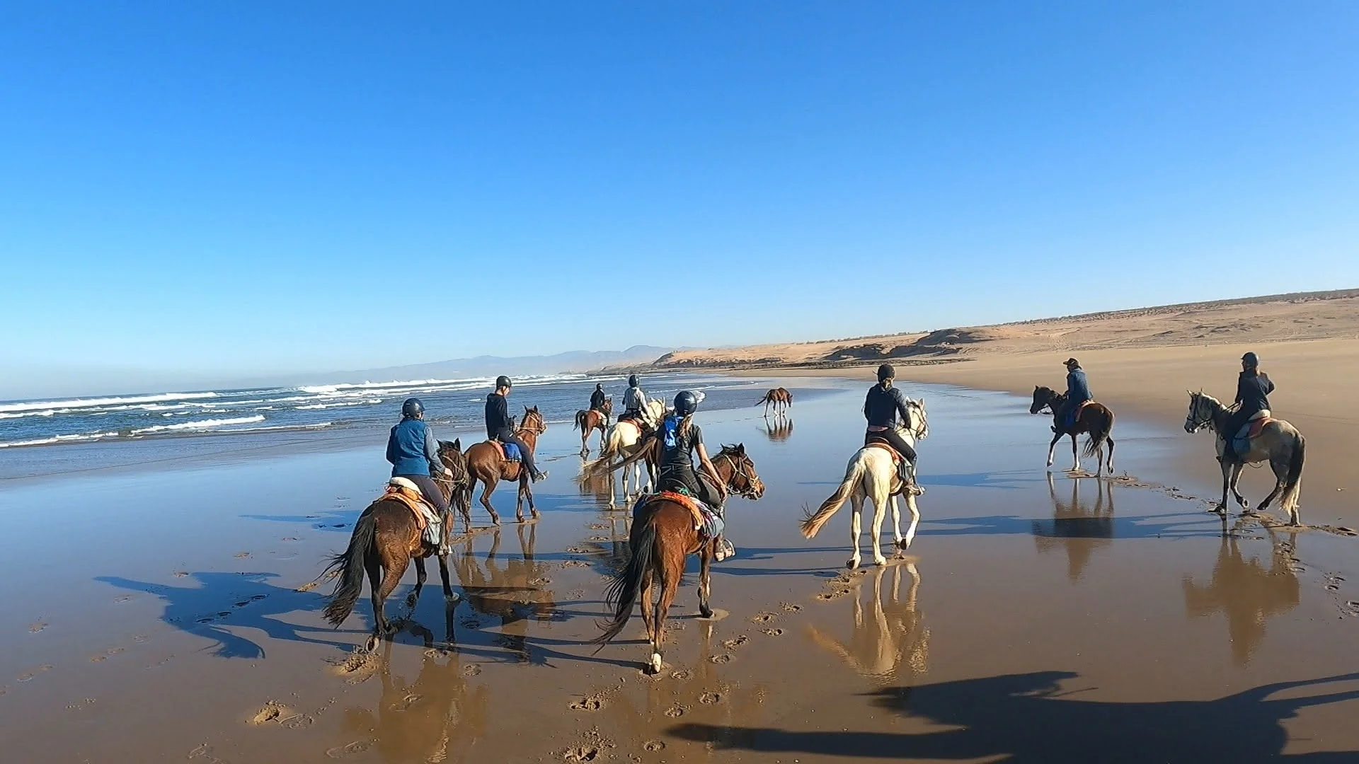 Reitergruppe am nassen Atlantikstrand mit Spiegelungen im Sand, links die Brandung, rechts die Dünen